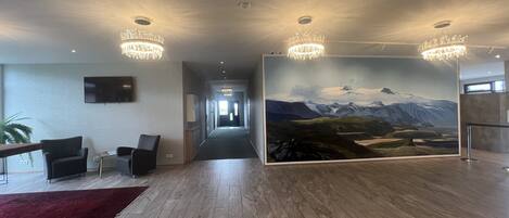 Un lobby moderno con piso de madera, alfombra roja, un gran mural de un paisaje montañoso y dos candelabros.