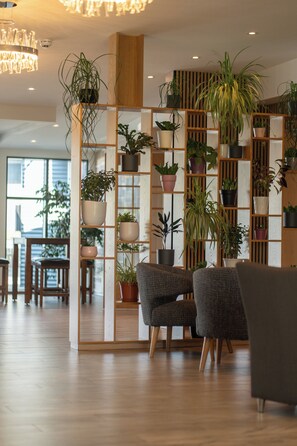 Un interior moderno con un separador de madera que sostiene varias macetas, dos sillones tapizados en gris y una araña.