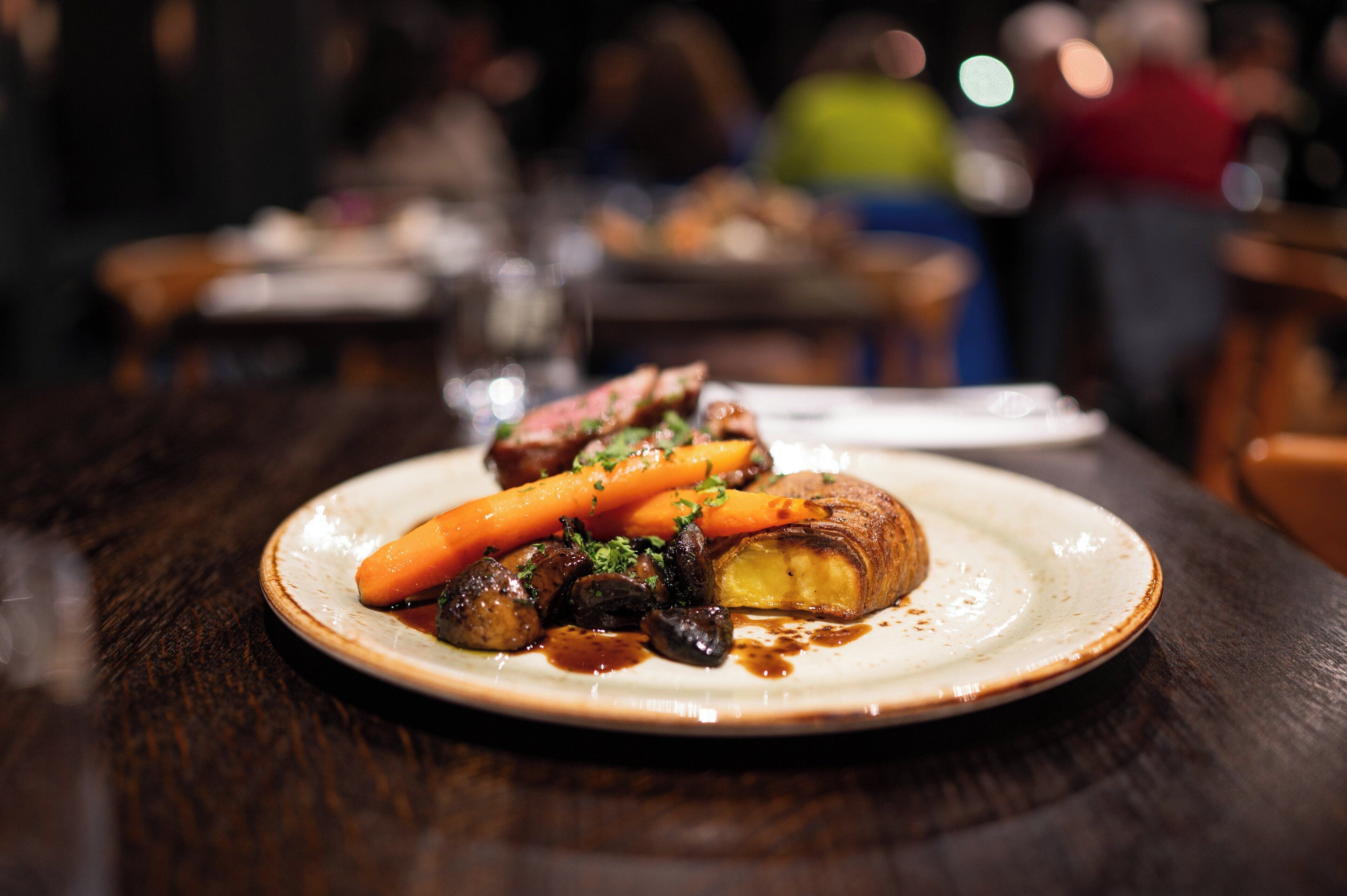 A plate of food with meat, carrots, and mushrooms on a table in a restaurant.