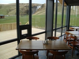 Un restaurante con vistas a una cascada, mesas y sillas de madera, y una terraza.
