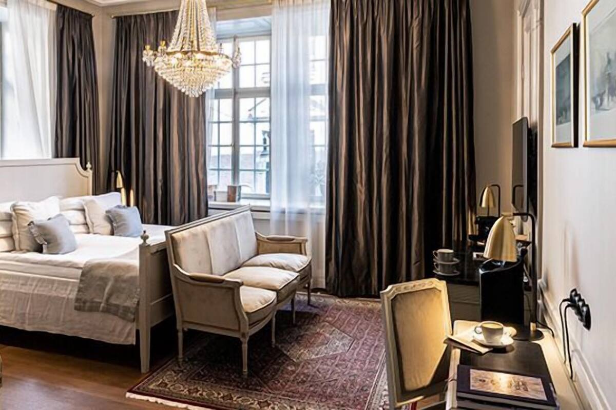Een slaapkamer met een groot bed, een slaapbank, een stoel, een salontafel en een kroonluchter.