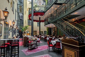 A restaurant with multiple dining tables, red upholstered chairs, and a staircase. - Hotel Kungsträdgården – The King´s Garden (Stockholm)