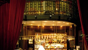 Una zona de bar con una barra curva, varios taburetes y una barandilla decorativa.