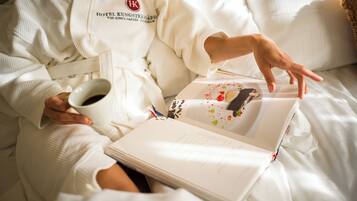 A person in a white robe holding a cup and a book with a dessert image on the cover.
