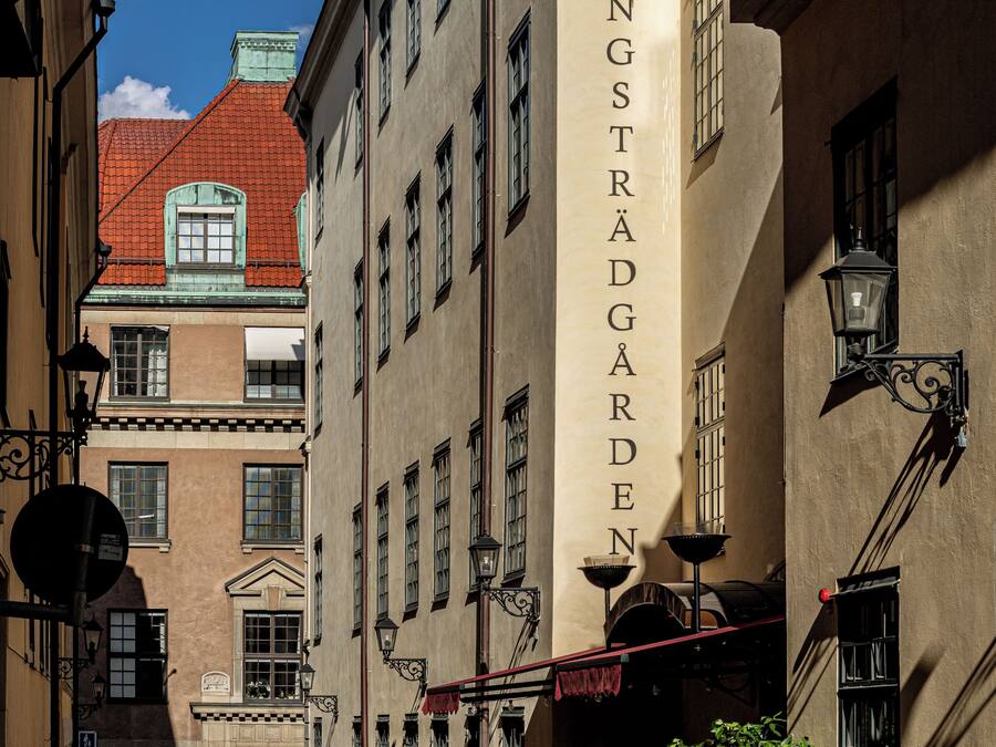 A cobblestone street with a vintage car parked in front of Hotel Kungsträdgården.