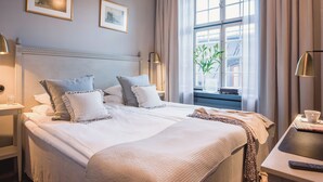 Habitación de hotel con una cama grande, dos mesitas de noche, una lámpara de noche, una ventana con cortinas y un candelabro.