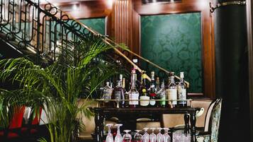 A bar area with a variety of bottles and glasses on a cart, a potted plant, and a staircase in the background.