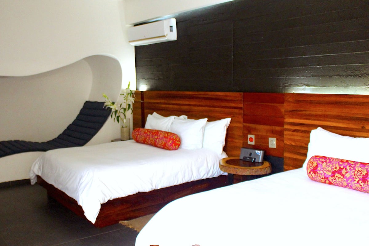 Habitación de hotel con un cabecero curvo único, una cama con sábanas blancas, una mesita de noche y un cabecero de madera.