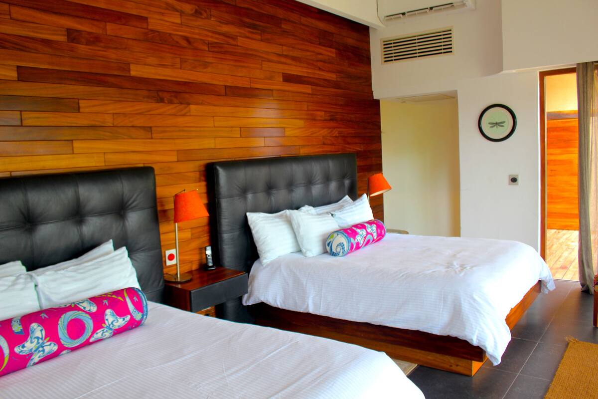 Habitación de hotel con dos camas, cabeceros de madera, ropa de cama blanca y suelo de madera.