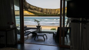 A room with a large glass door leading to a beach view, a television, and a seating area with a plant.
