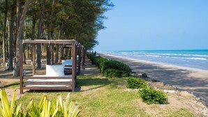 A wooden deck with a bench and a hammock overlooking a beach with trees and the ocean.
