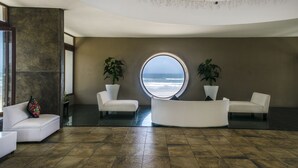 A modern interior with a circular window offering a view of the ocean, two white sofas, and potted plants.