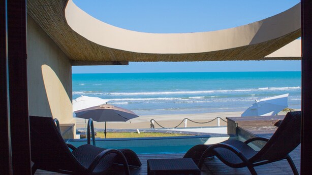 A poolside view with a beach and ocean in the background.