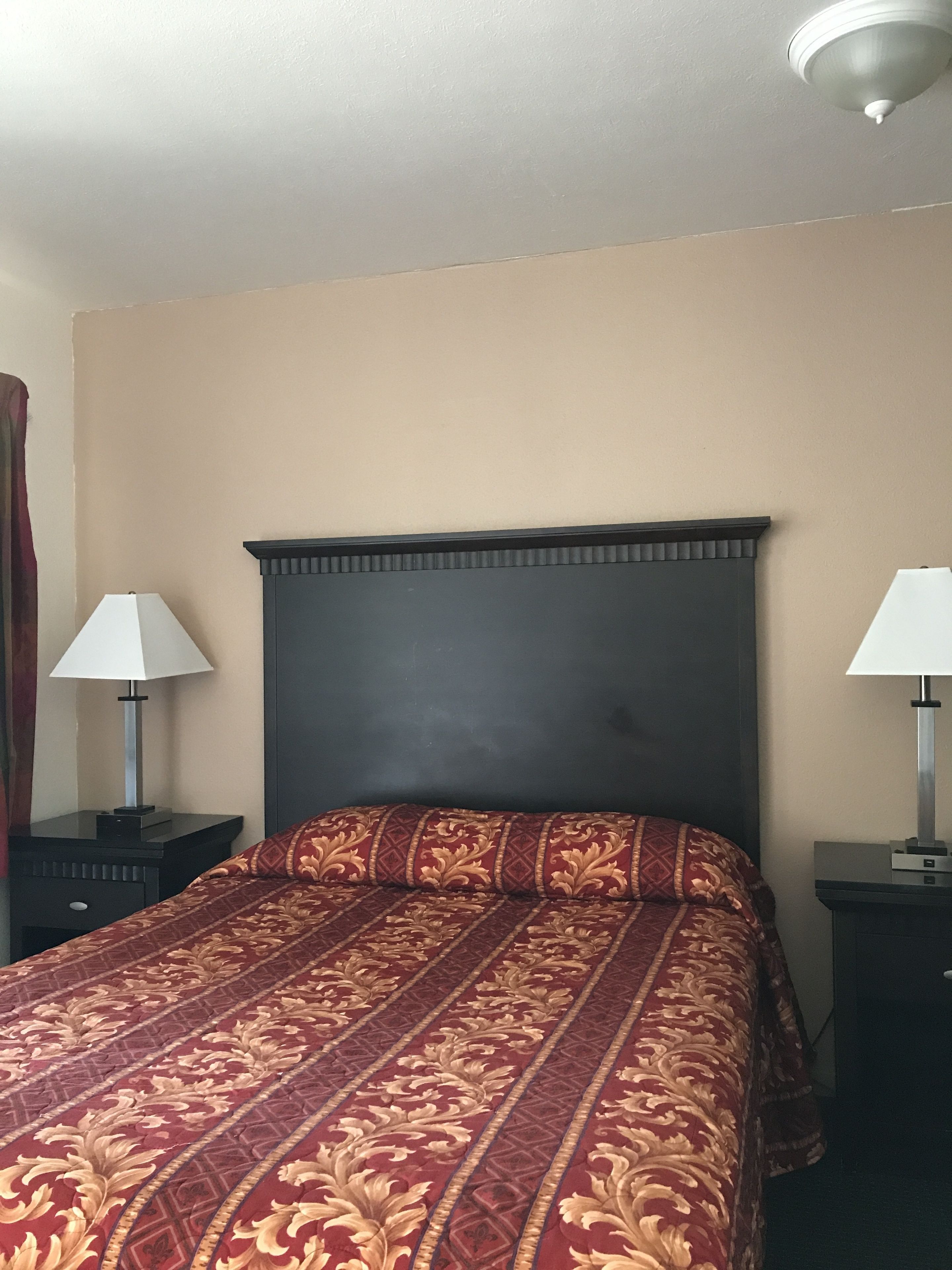 Ein Hotelzimmer mit einem Bett, zwei Nachttischen mit Lampen, einem dunklen Kopfteil und einer schlichten Wand.