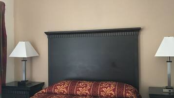 Ein Hotelzimmer mit einem Bett, zwei Nachttischen mit Lampen, einem dunklen Kopfteil und einer schlichten Wand.
