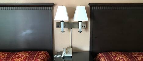 Habitación de hotel con dos camas, cada una con una colcha estampada en rojo y dorado. Hay dos mesitas de noche con lámparas, un teléfono y un cajón.