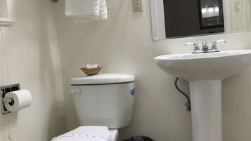 A bathroom with a toilet, a sink, a trash bin, a towel rack with towels, and a toilet paper holder.
