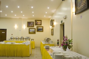 A banquet hall with tables set for a meal, framed pictures on the walls, and a fire extinguisher.