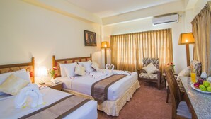 A hotel room with two beds, a sitting area, a dining table with fruit, and an air conditioning unit. - Reno Hotel (Yangon)