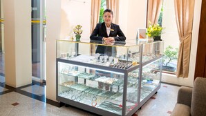 A jewelry display counter with a variety of items, a receptionist, and a sign reading "Reno Gems". - Reno Hotel (Yangon)