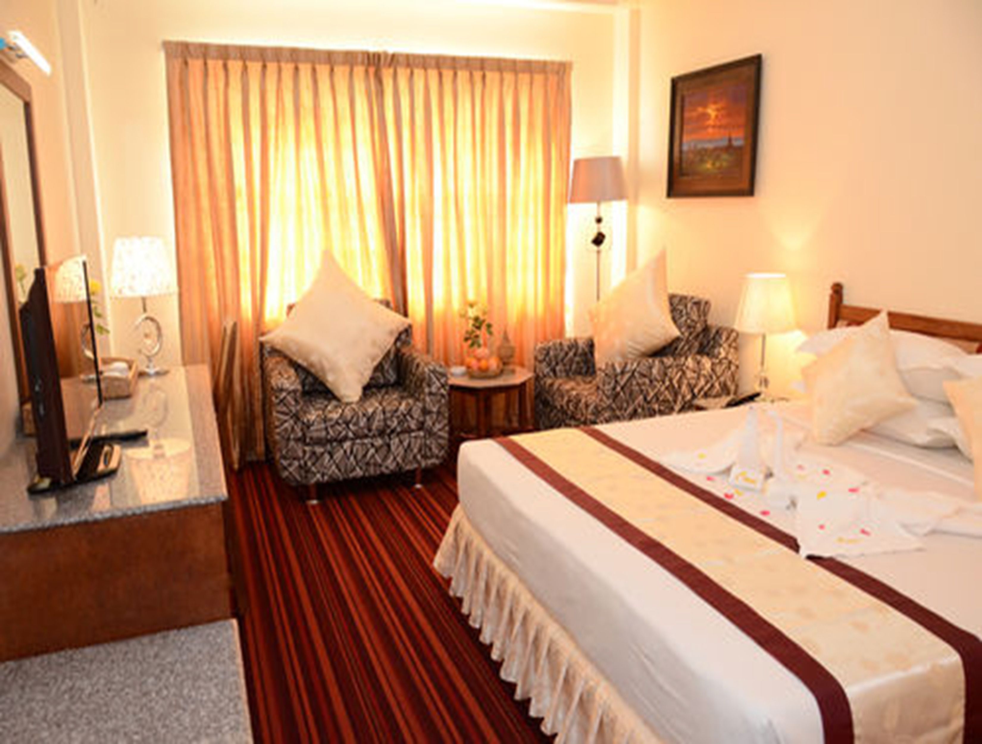 Una habitación de hotel con una cama grande, dos sillones, un escritorio con lámpara y un cuadro en la pared.