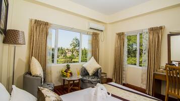 A hotel room with a bed, a desk, a chair, a table with fruits and a drink, and curtains.