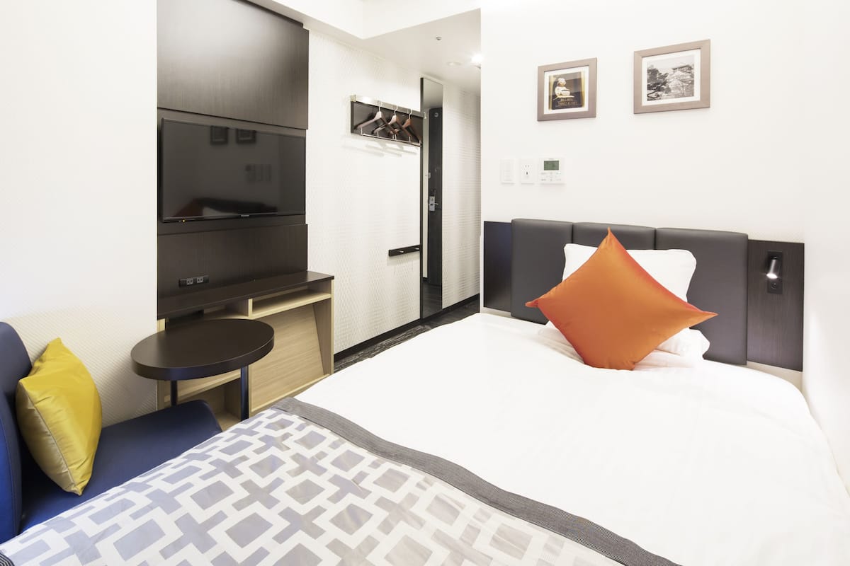 A hotel room with a bed, a TV, a desk, and a mirror.