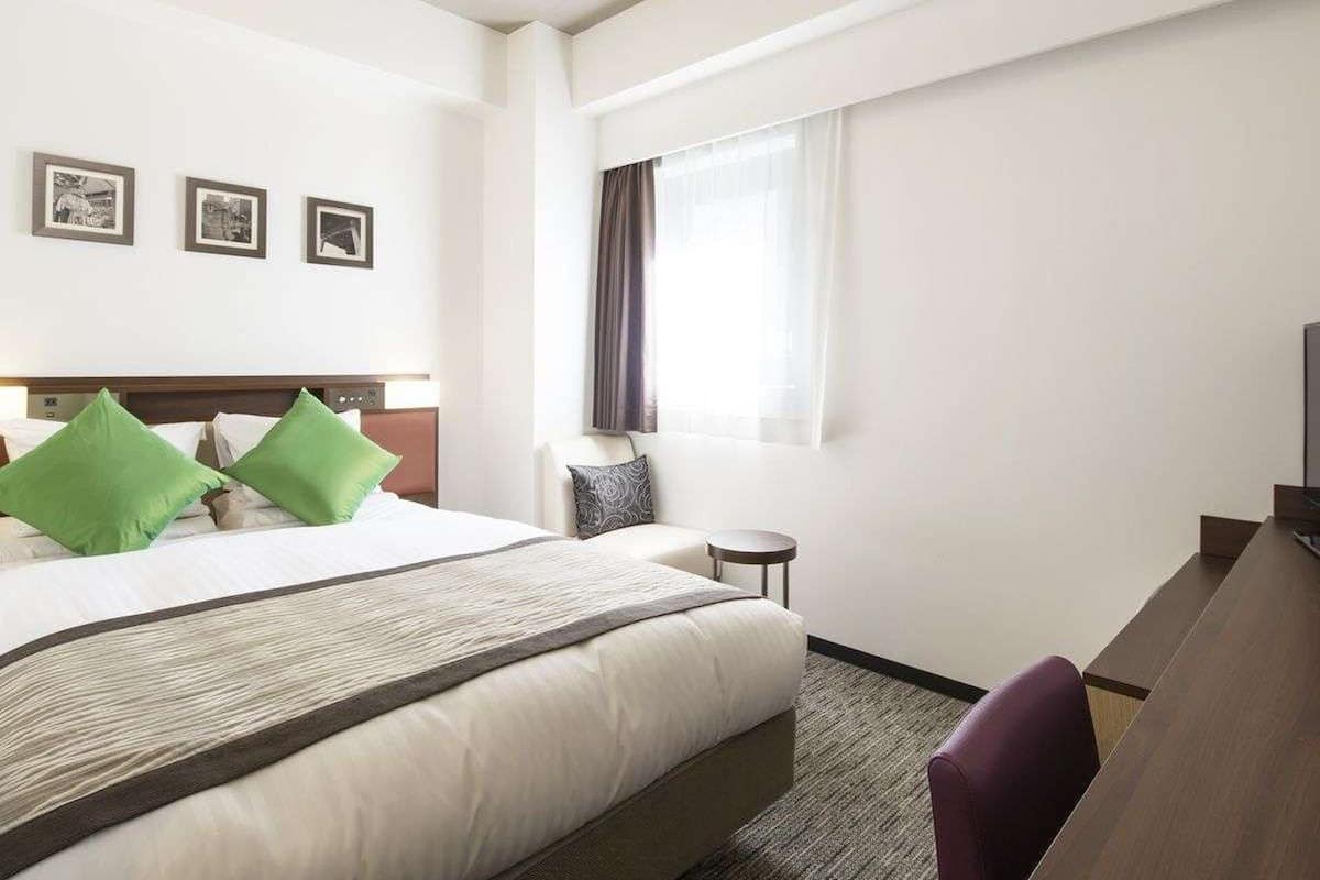 A hotel room with a large bed, a desk, a chair, a small table, and a window with curtains.