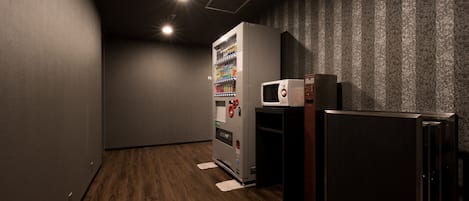 A compact room with a vending machine, microwave, and refrigerator.
