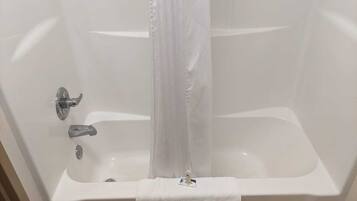 A white bathtub with a shower curtain, a towel, and a bottle of shampoo.