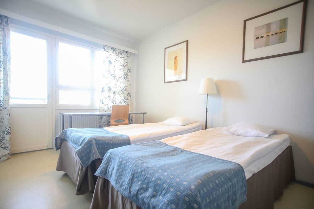 A hotel room with two beds, a desk, a chair, and a window with curtains.