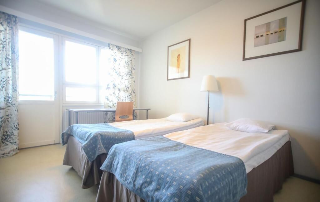Een hotelkamer met twee bedden, een bureau, een stoel, een lamp en twee ingekaderde foto's aan de muur.