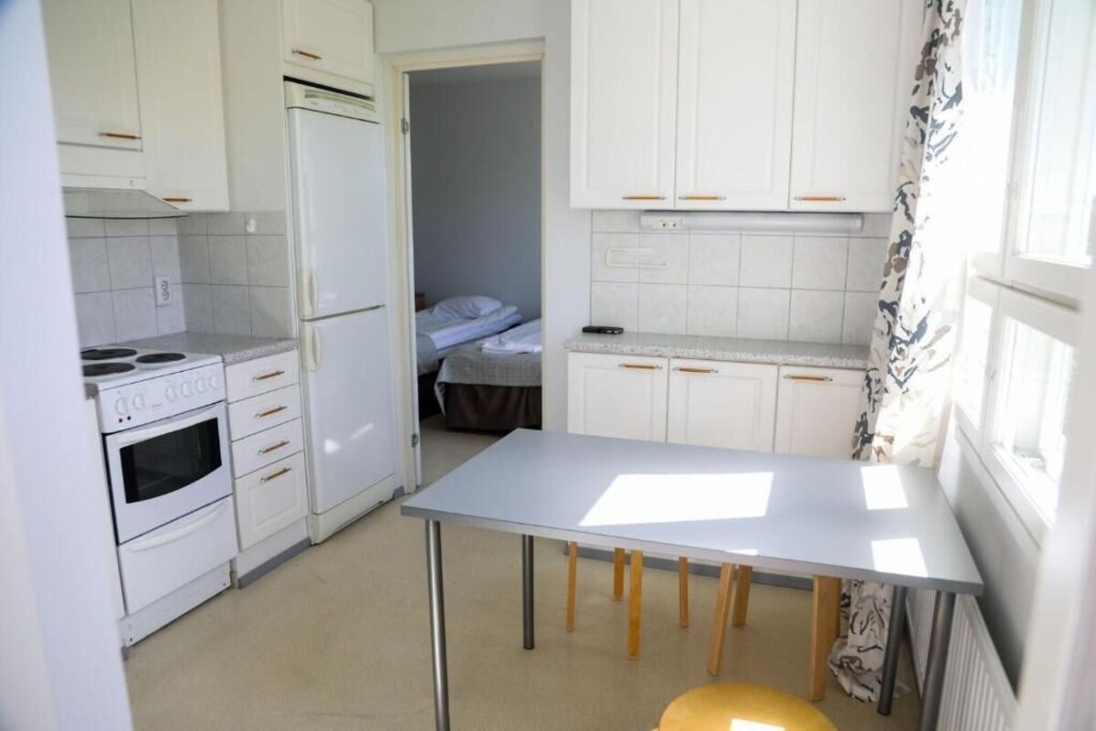 Eine kleine Küche mit weißen Schränken, einem eingebauten Backofen und einem Tisch.