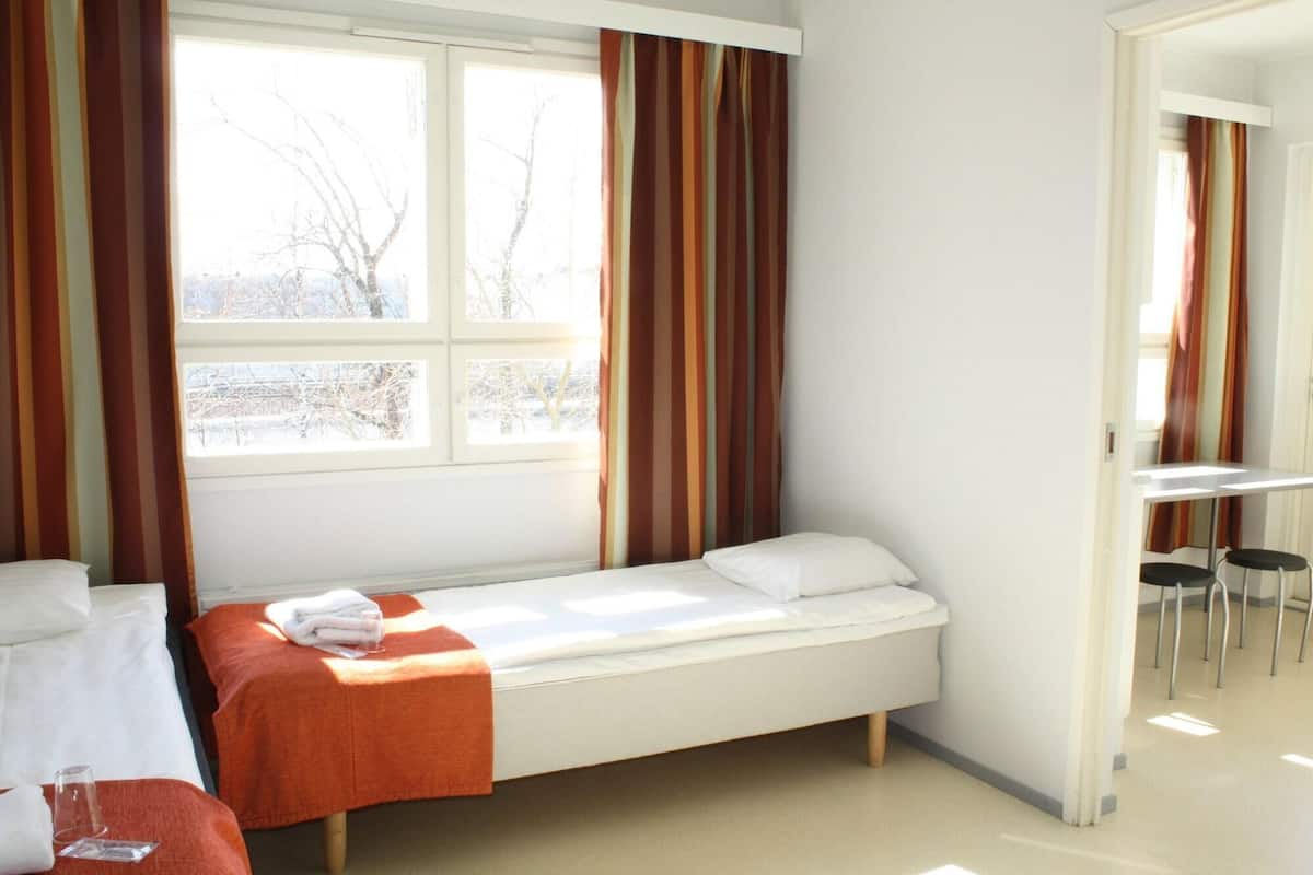 A single-bed room with a window, a small table, and chairs.