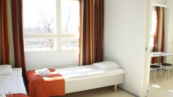 A single-bed room with a window, a small table, and two chairs.