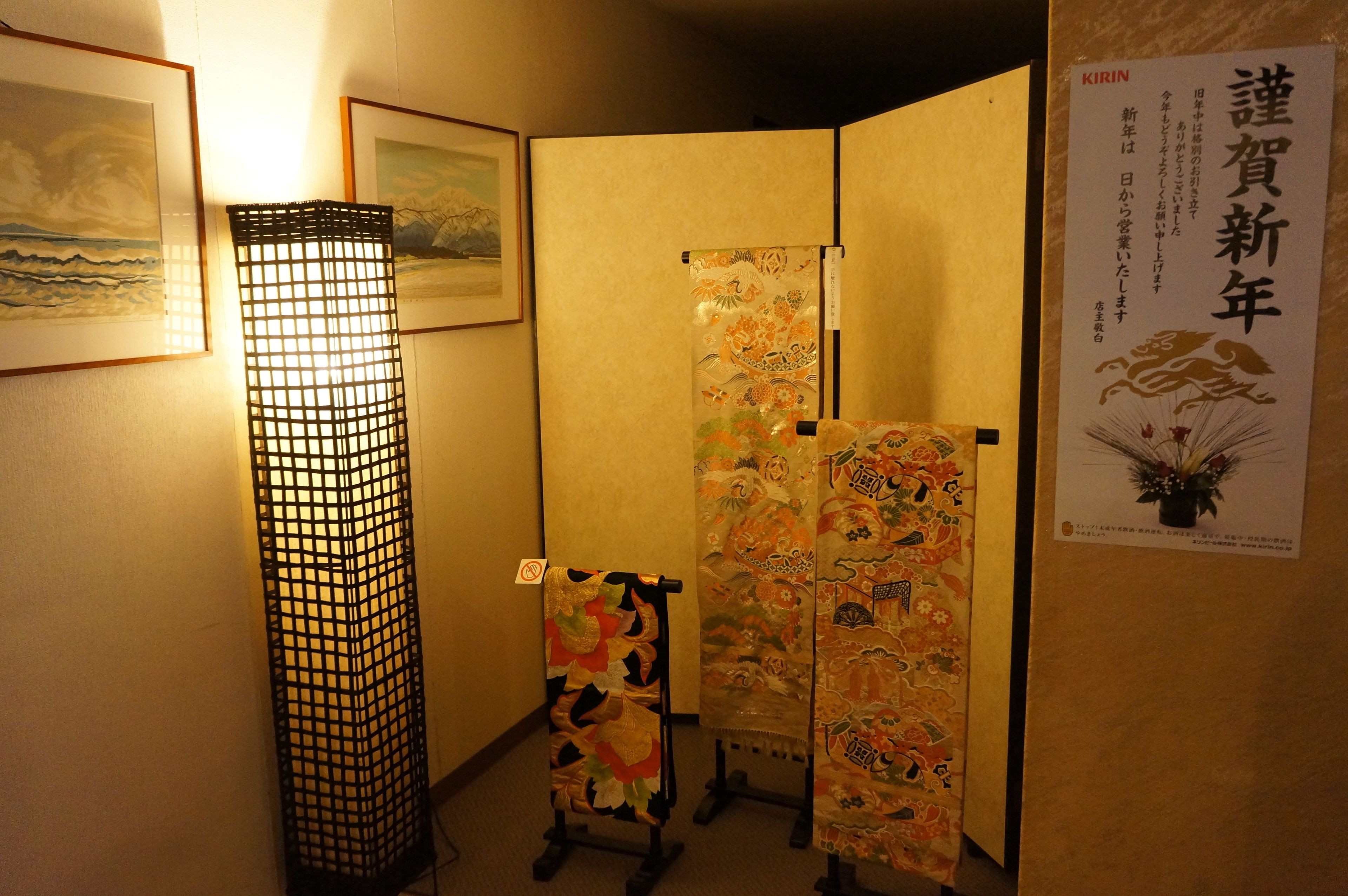 Huoneessa on perinteinen japanilainen shoji-seinä, lattiavalaisin ja seinällä olevia taideteoksia kehyksissä.