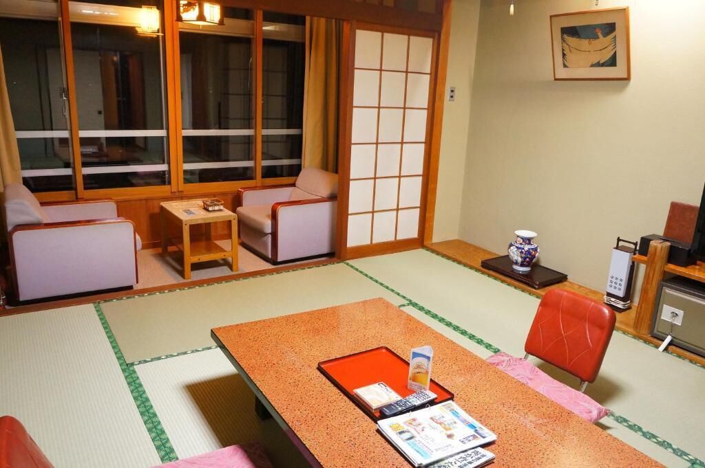 Ein traditioneller japanischer Raum mit Tatami-Böden, einem niedrigen Tisch mit Tablett, zwei gepolsterten Sitzbereichen und einer Schiebetür.