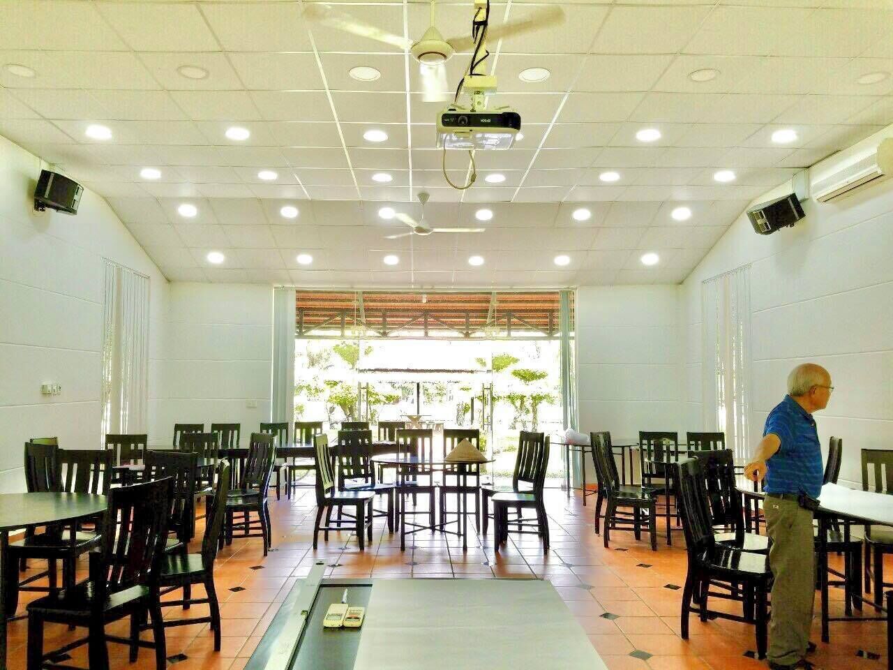 A dining area with tables and chairs, ceiling fans, and a projector.