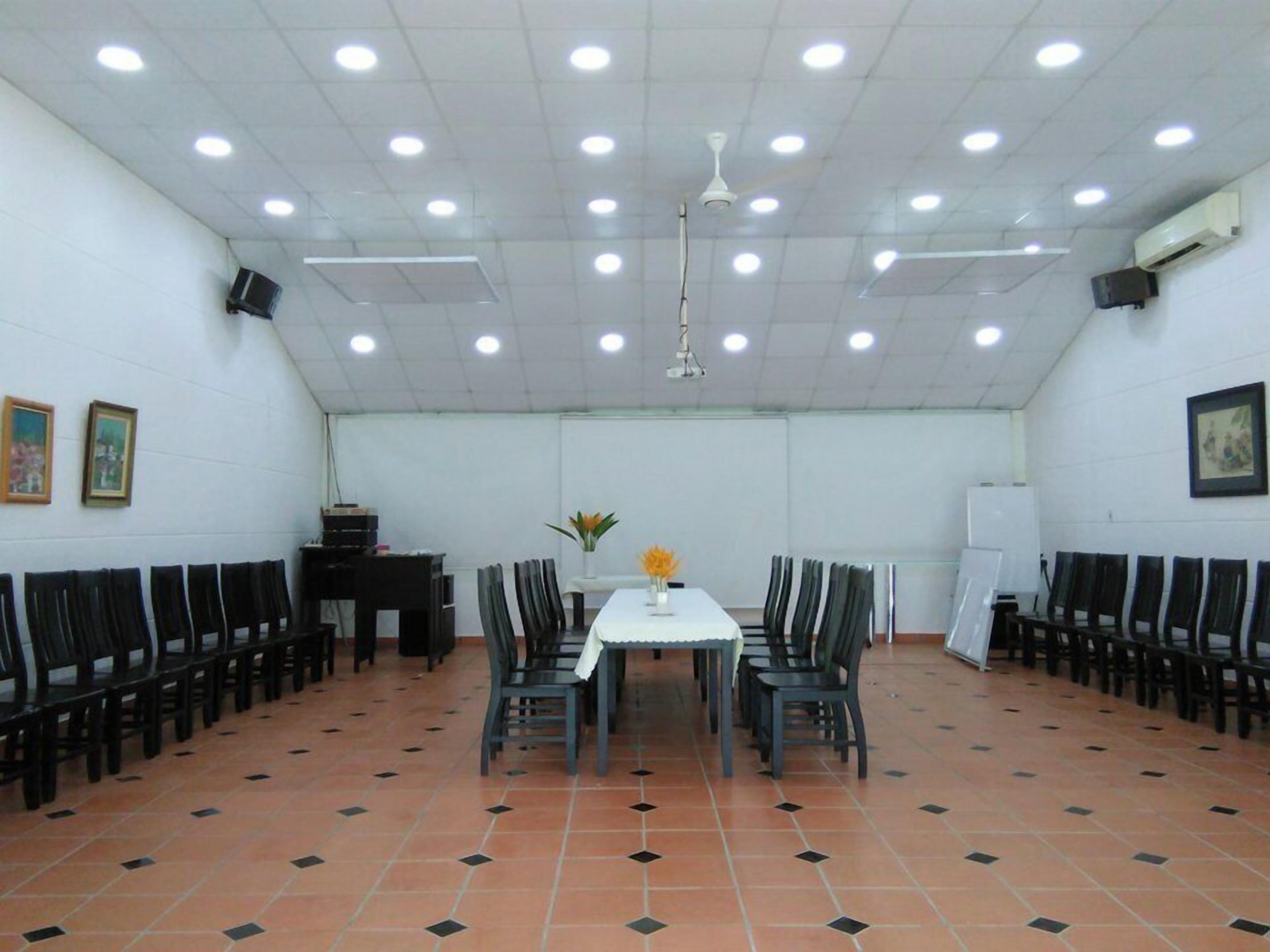 Un salón de conferencias con una larga mesa, sillas, luces de techo y una pizarra.