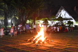 Eine gesellige Runde im Freien mit einem Feuer in der Mitte, umringt von Menschen.