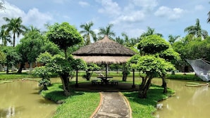 A thatched-roof pavilion surrounded by a pond, with a pathway leading to it. - Les Hameaux de l'Orient (Ho Chi Minh City)