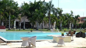 A pool area with lounge chairs and tables, surrounded by palm trees and a building with a tiled roof. - Les Hameaux de l'Orient (Ho Chi Minh City)