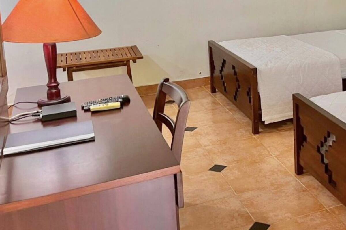 Hotellihuone, jossa on kaksi erillistä sänkyä, puinen työpöytä, tuoli ja lamppuvarustettu pöytä.