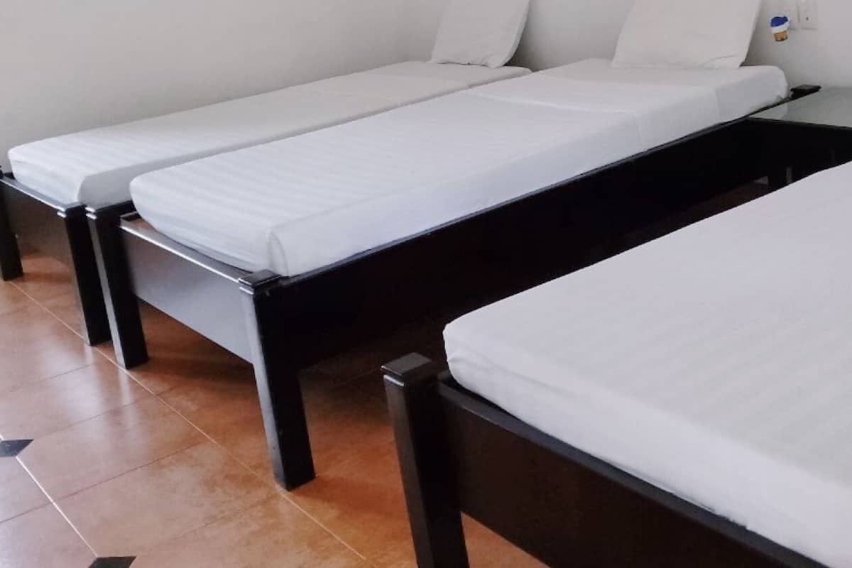 Hotellihuone, jossa on kolme erillistä sänkyä, ja jokaisessa on valkoinen patja ja musta sängynrunko.
