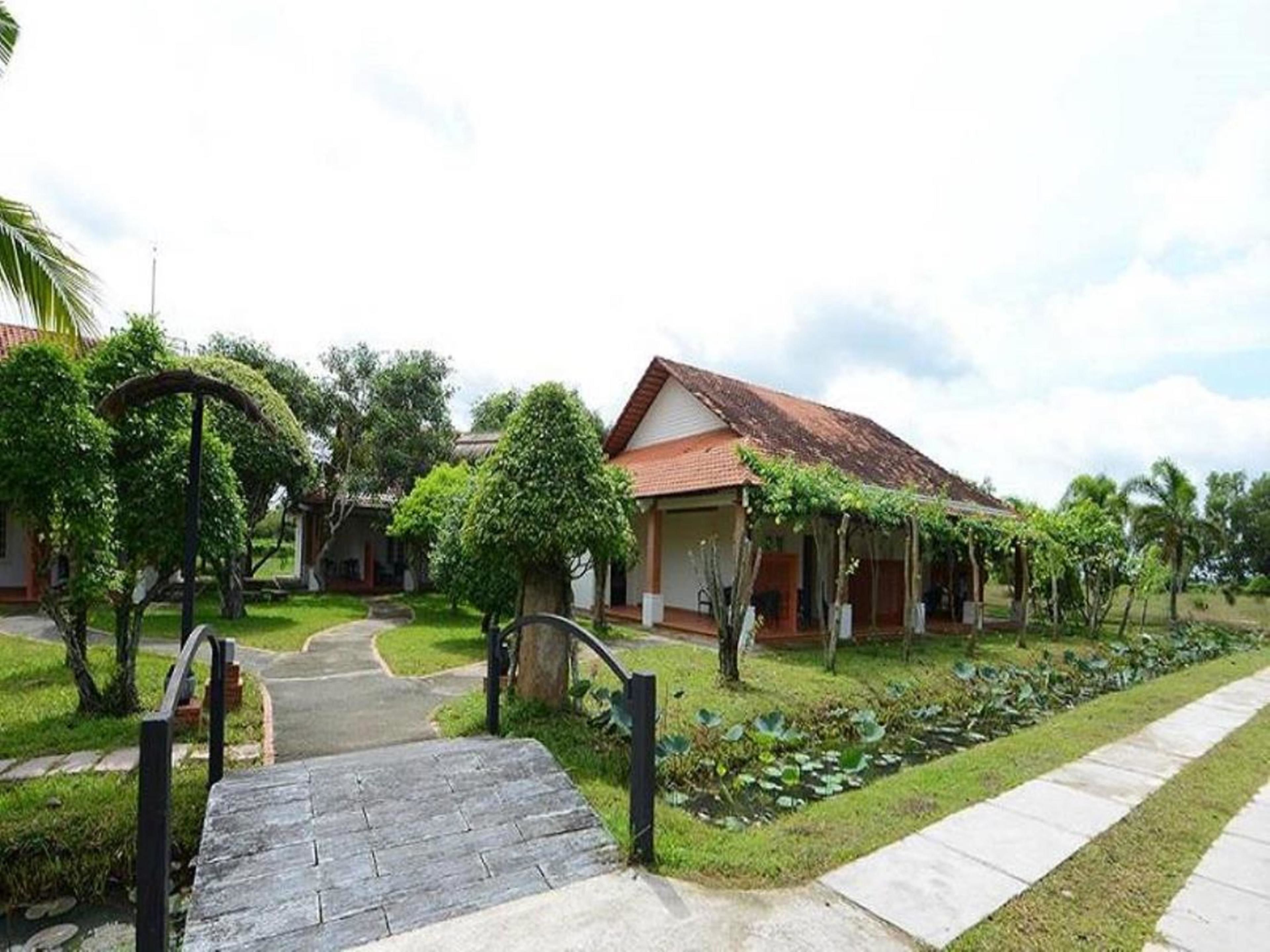 A traditional house with a tiled roof, surrounded by lush greenery and a paved pathway leading to the entrance.