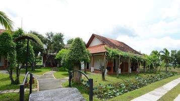 A traditional house with a tiled roof, surrounded by lush greenery and a paved pathway leading to the entrance.