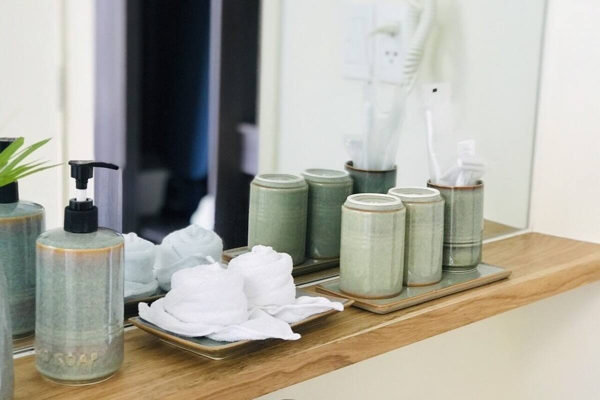 Un tocador de baño con encimera de madera, un espejo y artículos de aseo como dispensador de jabón, toallas y tarros.