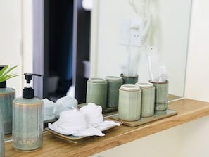 Un tocador de baño con encimera de madera, un espejo y artículos de aseo como dispensador de jabón, toallas y tarros.