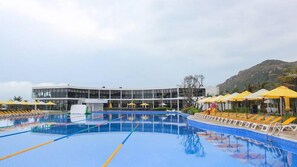 Una piscina con un edificio moderno al fondo, rodeada de sombrillas amarillas.