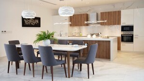 A modern kitchen with a central island, wooden cabinets, and a dining area with a marble table and chairs. - Viva Villa Oceanami (Nam Nha Trang)